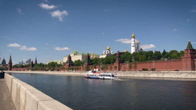 Moscow. Kremlin Embankment. Red Brick Wall Along the River. Green Trees Behind the Fence. Concrete Banks. Gold Top Church. Floating Ferry. Wide Shot