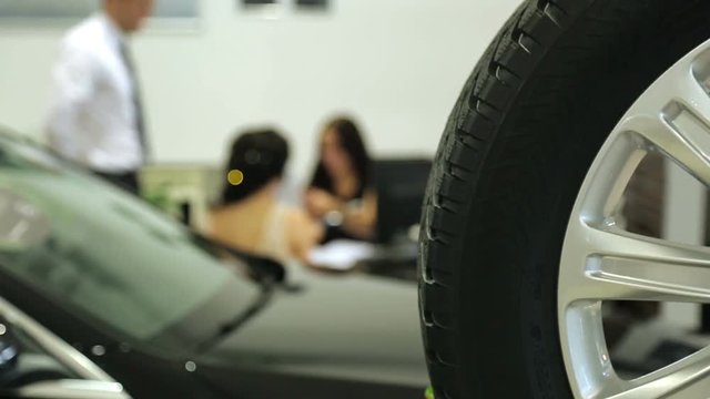 Work in the showroom. Sales Manager at the dealership works at a Desk. In the foreground of the car and wheel , the image Manager is blurred.