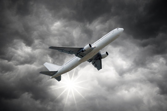 Airplane above Dark storm sky and shining Sun