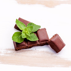 pieces of chocolate with mint on white wooden background