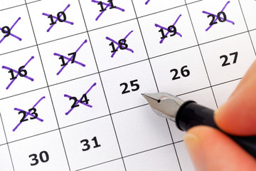 Fountain pen in person hand marking days on calendar