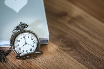 Naklejka premium Luxury pocket watch over the book on the wooden table with copy space