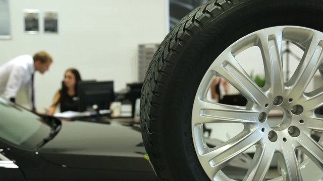 Work in the showroom. Sales Manager at the dealership works at a Desk. In the foreground of the car and wheel , the image Manager is blurred.