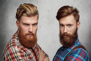 Two handsome young unshaved men with hipster beards dressed in stylish checkered shirts, standing...