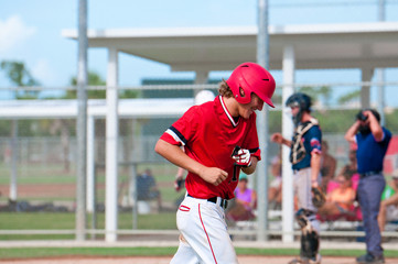 Happy teen baseball player running off field smiling.