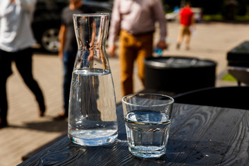 A glass of water and a water-bottle on a black wooden table of a city cafe terrace