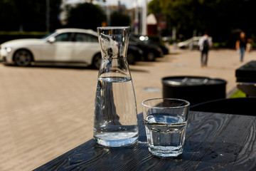 A glass of water and a water-bottle on a black wooden table of a city cafe terrace