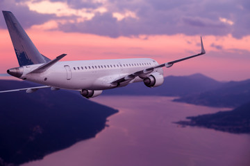 Airplane flying at purple sunset over mountains and sea