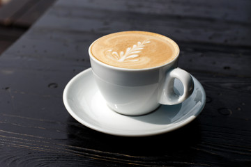 A white cup of cappuccino on the dark wooden table