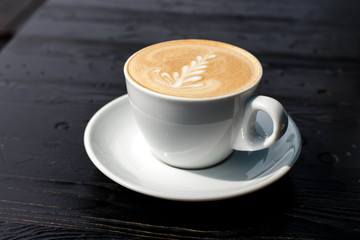 Fototapeta premium A white cup of cappuccino on the dark wooden table
