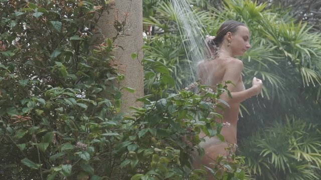 Woman having shower and washing hair in the garden, slow motion shot