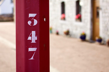 Pfahl mit aufgedruckter Zahl 347 im Vordergrund und Haus im unscharfem Hintergrund