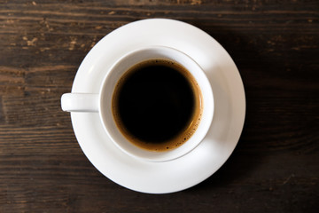 A white cup of black coffee on the wooden table. Selective focus, small depth of fieild.