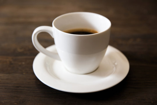 A white cup of black coffee on the wooden table. Selective focus, small depth of fieild. © jamurka