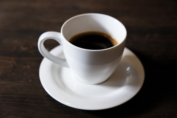 A white cup of black coffee on the wooden table. Selective focus, small depth of fieild.