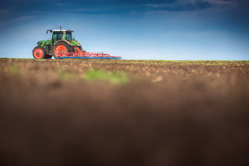 Fototapeta premium Farmer in tractor preparing land with seedbed cultivator