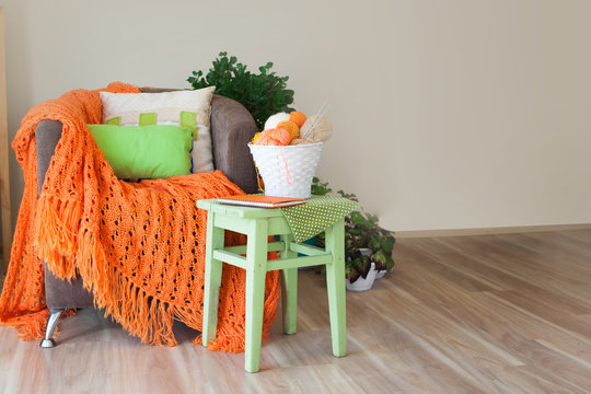 Skeins of wool lying in a white basket. Orange knitted blanket.