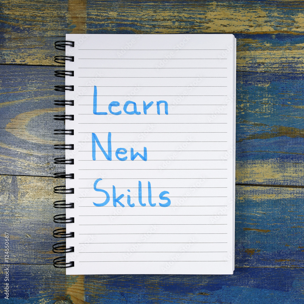 Aufkleber learn new skills written in notebook on wooden background