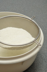 Sifting flour into a white plastic bowl