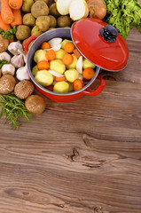 Red casserole dish stew pot or dutch oven lid open with winter vegetables and herbs for soup on wood kitchen counter worktop photo