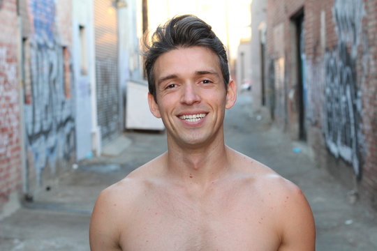 Sexy smiling shirtless male model flirting against alleyway urban background