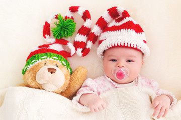 Baby girl in a Christmas hat with her teddy bear