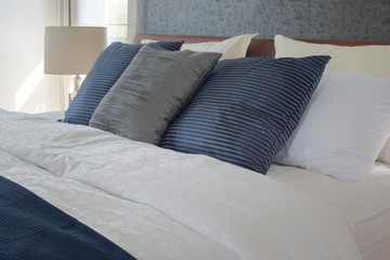Gray and deep blue pillows on bed and white reading lamp in background