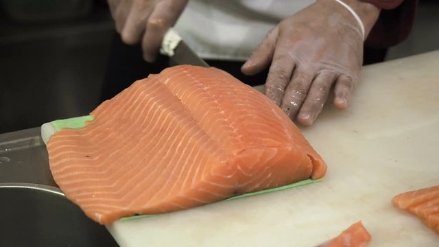 Process of making and cutting salmon for sushi rolls. Cook cutting up fish by knife on thin slices.