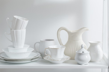 Fototapeta na wymiar Clean dishes and vases on white wooden shelf
