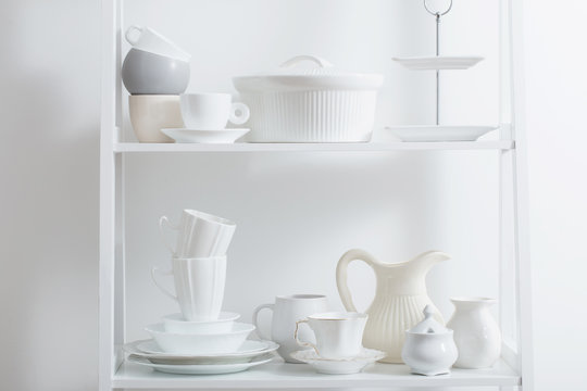 Clean dishes and vases on white wooden shelf