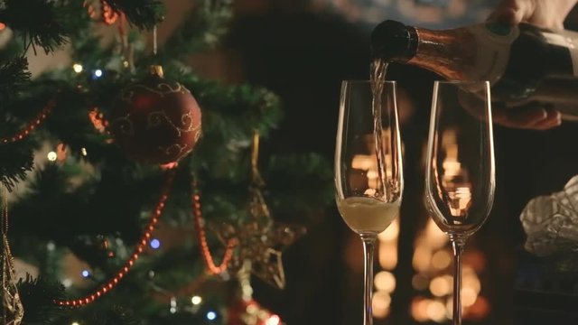 Pour the champagne into the glasses on the background of the Christmas tree and fireplace. Christmas party