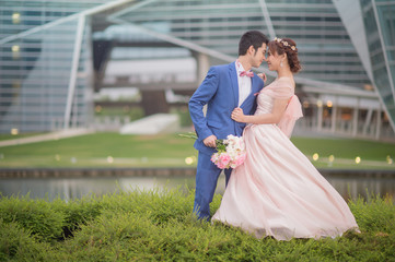 Happy newlywed groom hugging and kissing blonde beautiful bride at sunset in city