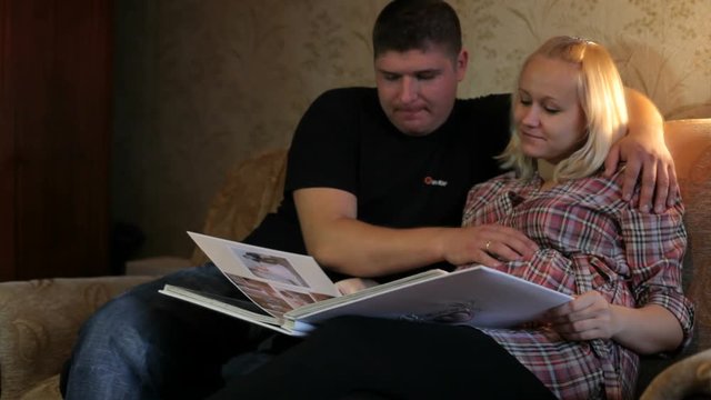 A pregnant woman with her husband looking photo album.