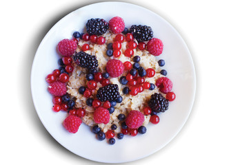 Oatmeal with raspberries, blackberries, red currant and blueberries in a white plate on white background