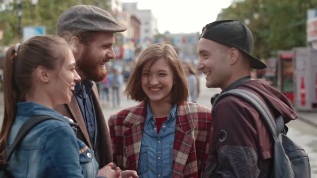 Group of young laughing friends standing on street chatting and taking selfie 