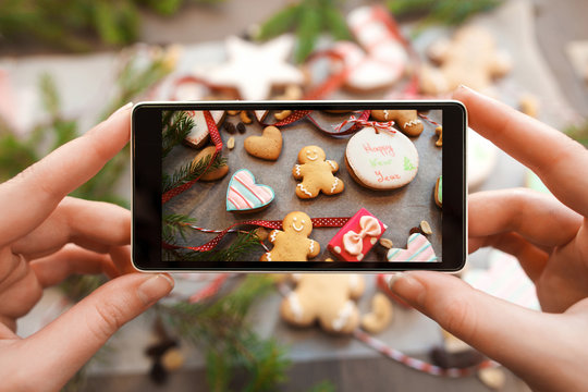 Hands taking picture of gingerbread cookies. Close-up photo of smartphone photographing traditional Christmas treat assortment. Food photography concept