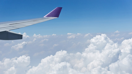 View from window with wing of airplane flying above the clouds