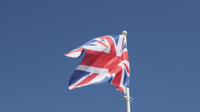 National Great Britain symbol Union Jack waving on flag-pole against blue sky 4K 2160p 30fps UHD footage - Flag of United Kingdom floating on wind 3840X2160 UltraHD video 