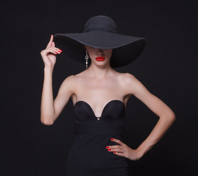Luxury woman in a large black hat and bright lips on black background