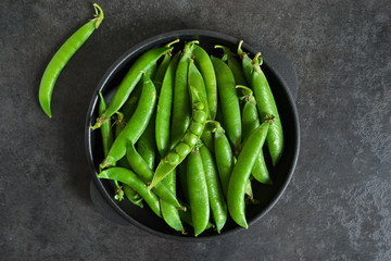 Green, young peas in a cast-iron plate on a black background