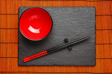 Two chopsticks and red plate on black stone background with copyspace