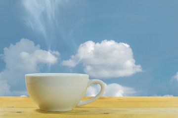 Close up of the white coffee mug on a wooden floor with the blue sky background.