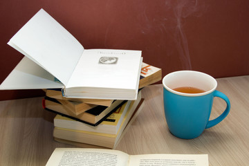 a stack of books and a hot drink in a blue mug on wooden table,