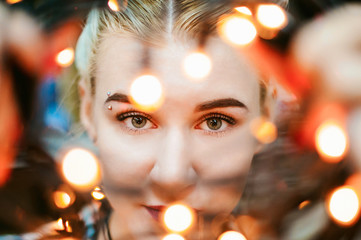 Portrait of a young woman with lights. beautiful girl with white hair dyed, looking through the Christmas lights