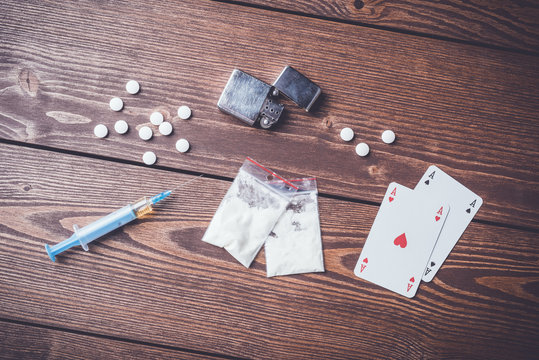Hard drugs with pills, playing cards and syringe on wooden table