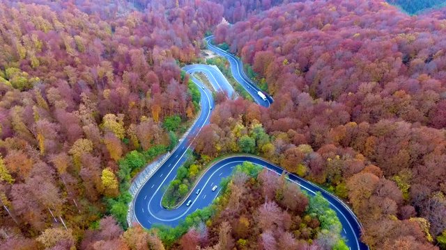 Winding road trough the forest. Hi mountain pass in Transylvania, Romania. Aerial view from a drone. Cars traveling on the road.