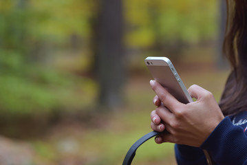 Woman holding mobile phone and headphones in hand against a blurry autumn forrest background