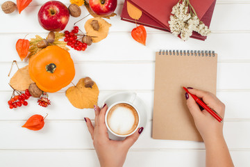 Naklejka na ściany i meble Autumn background. Female hand writing in notebook near cup of cappuccino.
