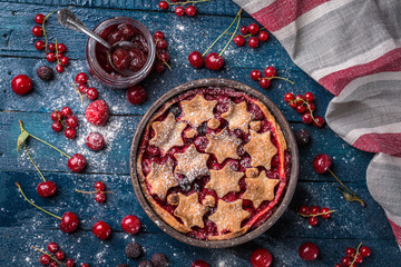Berry pie decorated with stars, jam, sugar powder and berries on the navy-blue background with kitchen towel