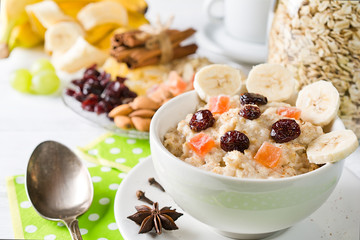  Oatmeal porridge with dried fruits, cranberries, bananas and spices. Jar of oatmeal on background. Arranged on white background.
